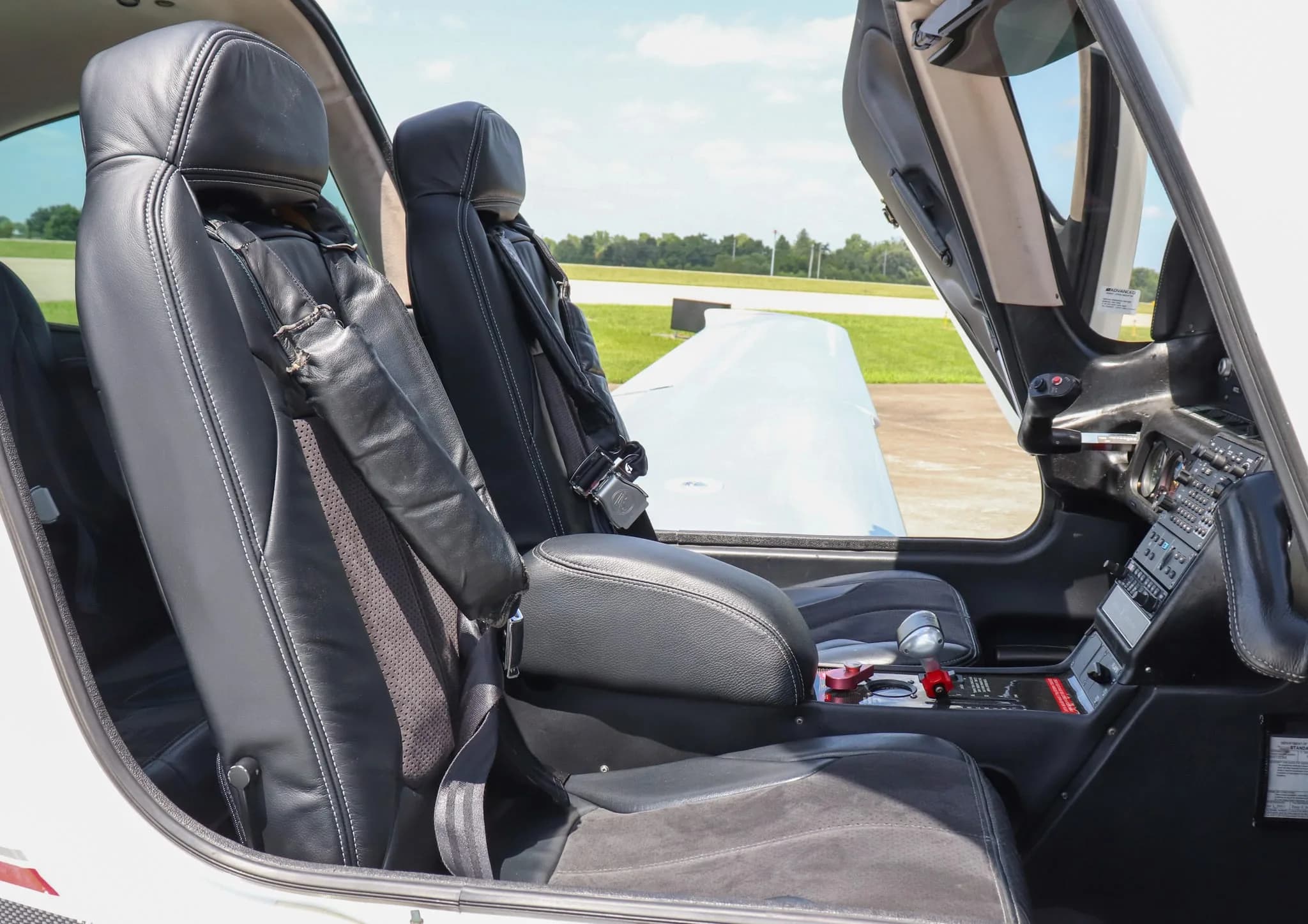 The black leather front seats of the Cirrus SR20 with the pilot's door open on an airfield.