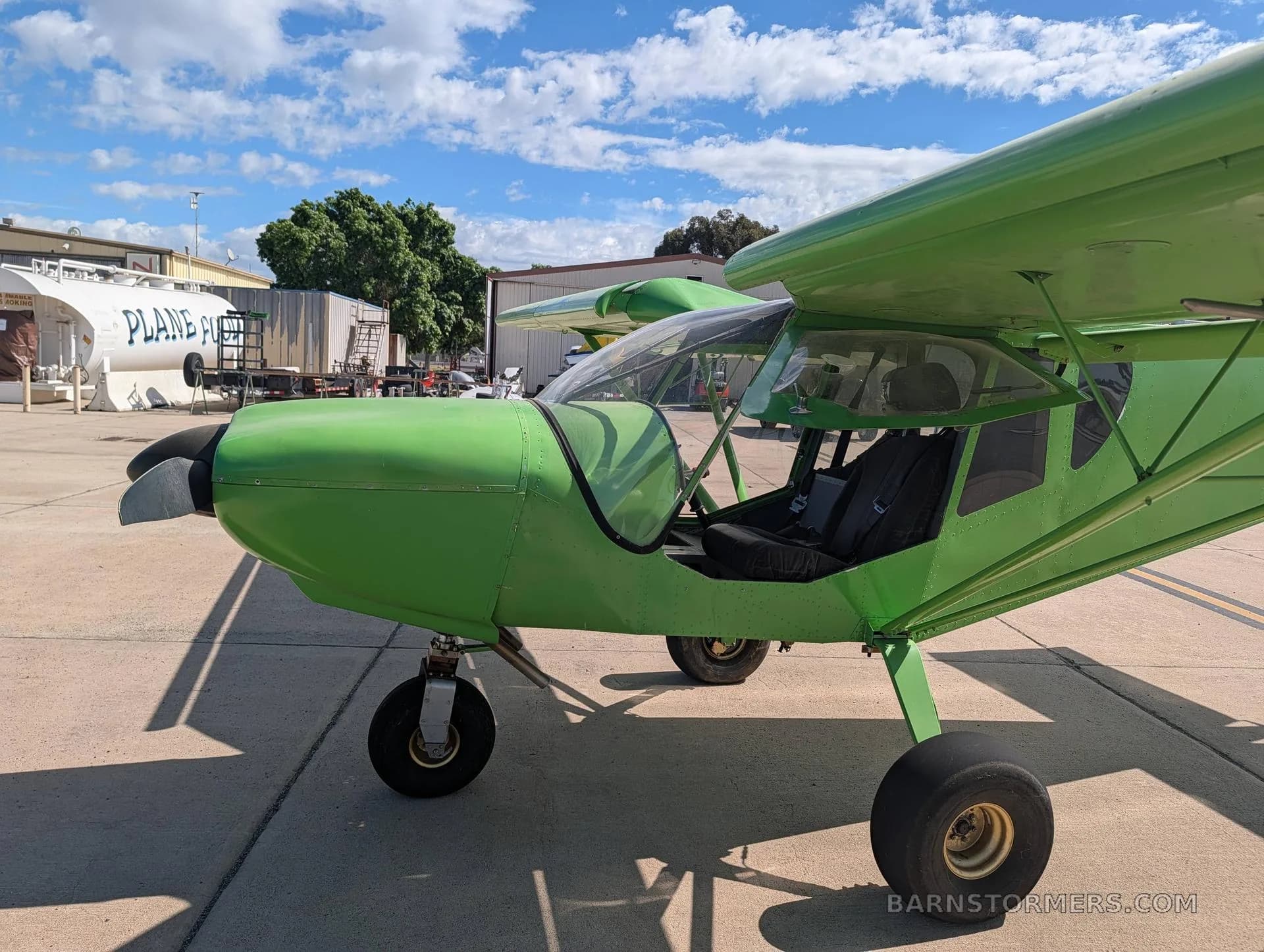 A close-up side view of the bright green Zenith STOL CH 750 aircraft on an airfield, showing the propeller and front landing gear.