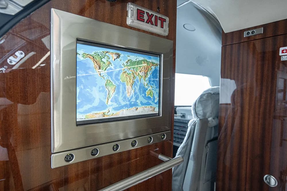 An in-cabin display screen showing a world map, mounted on a wood-paneled wall near an exit sign.
