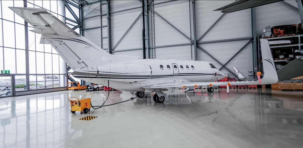 A white business jet with grey stripes parked inside a large, well-lit hangar.
