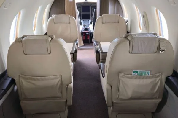 The aircraft's interior cabin with light-colored seats, viewed from the rear towards the cockpit.