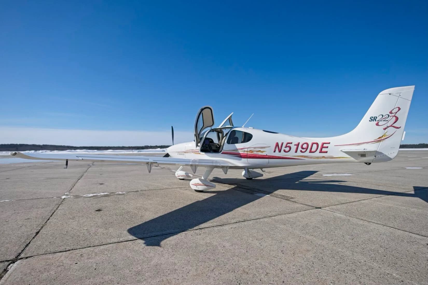 A white Cirrus SR22 aircraft with red and gold decals, registration N519DE, parked on a tarmac with both cabin doors open.