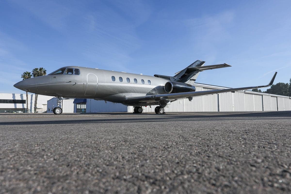 Side view of a red and silver single-engine aircraft parked on the tarmac.