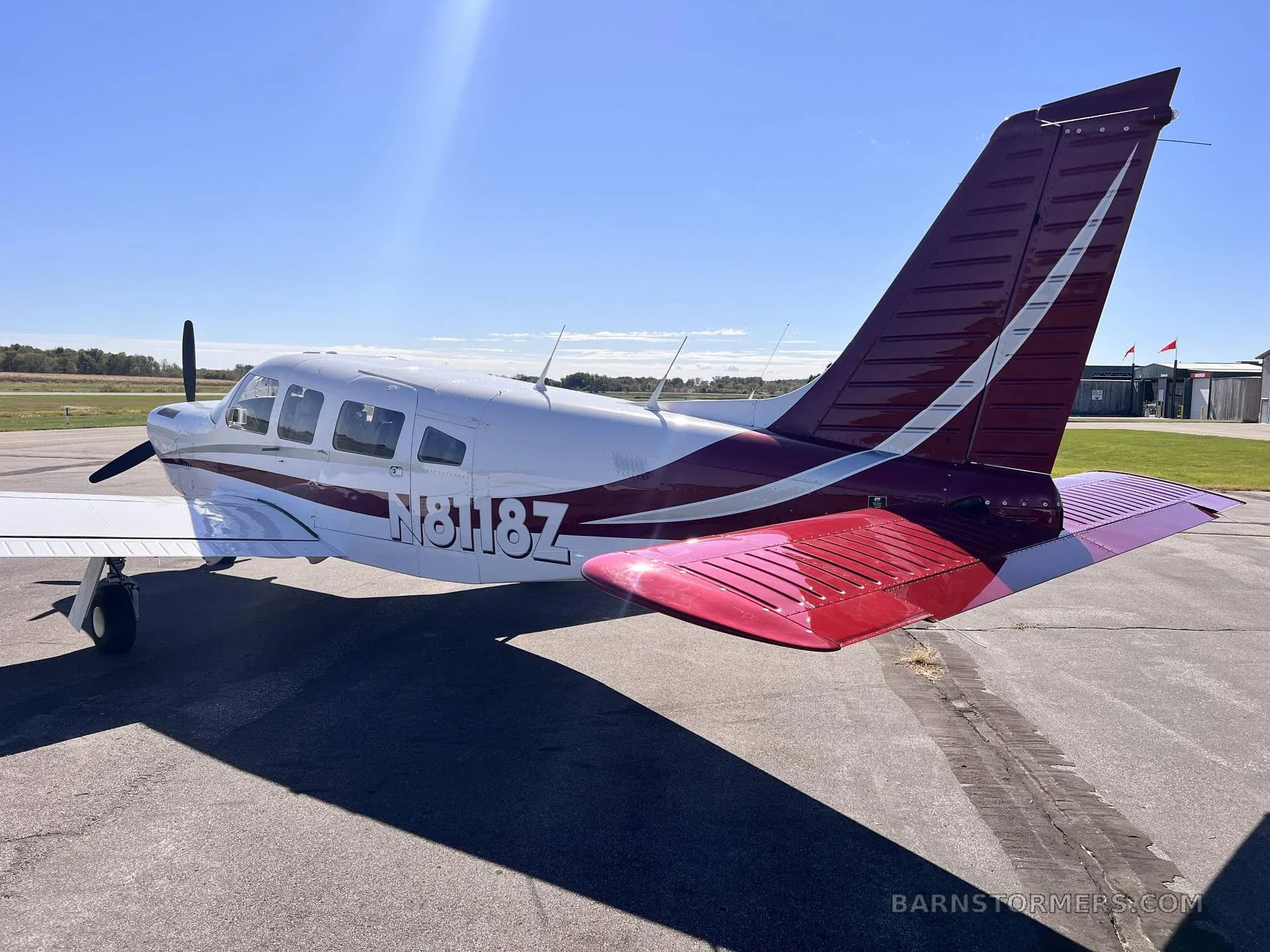 The rear-left view of a white single-engine propeller aircraft with a red and white tail, registration N8118Z, parked on an asphalt ramp.
