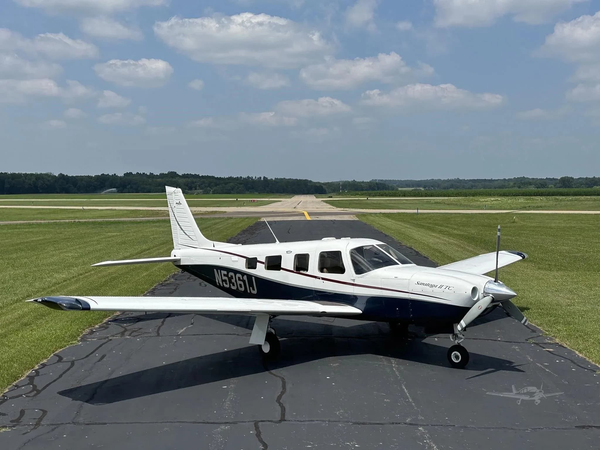 A white and blue Piper Saratoga II TC (N5361J) is parked on an asphalt runway under a partly cloudy sky.