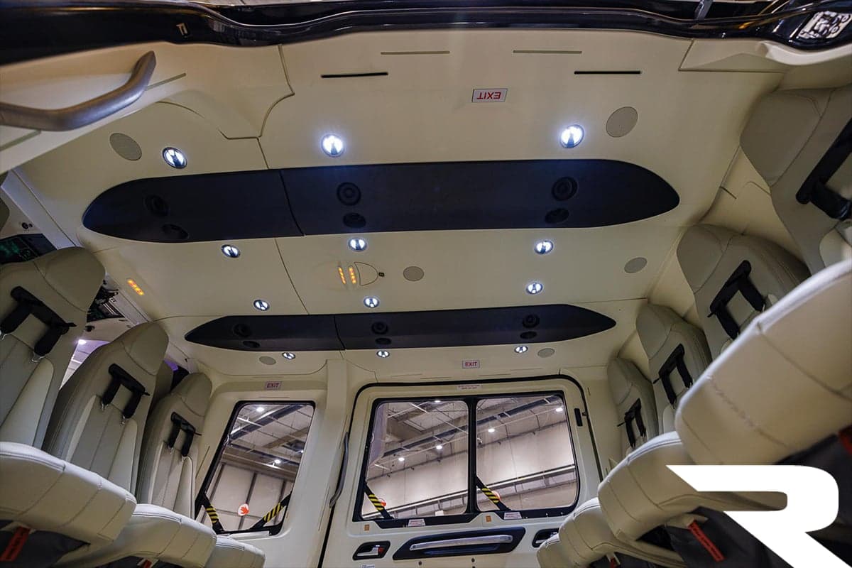 The interior cabin ceiling and windows of an Airbus H160 helicopter, showing overhead lights and exit signs.