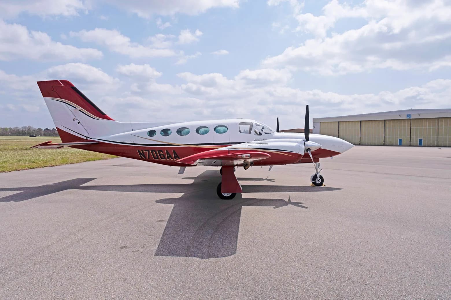 A side view of a white and red Cessna 421C Golden Eagle with registration N706AA parked on an airfield.