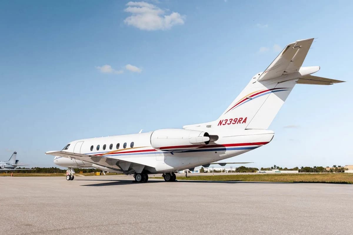 The rear-side view of a white Hawker 800XP business jet with red and blue stripes, registration N339RA, parked on the tarmac.