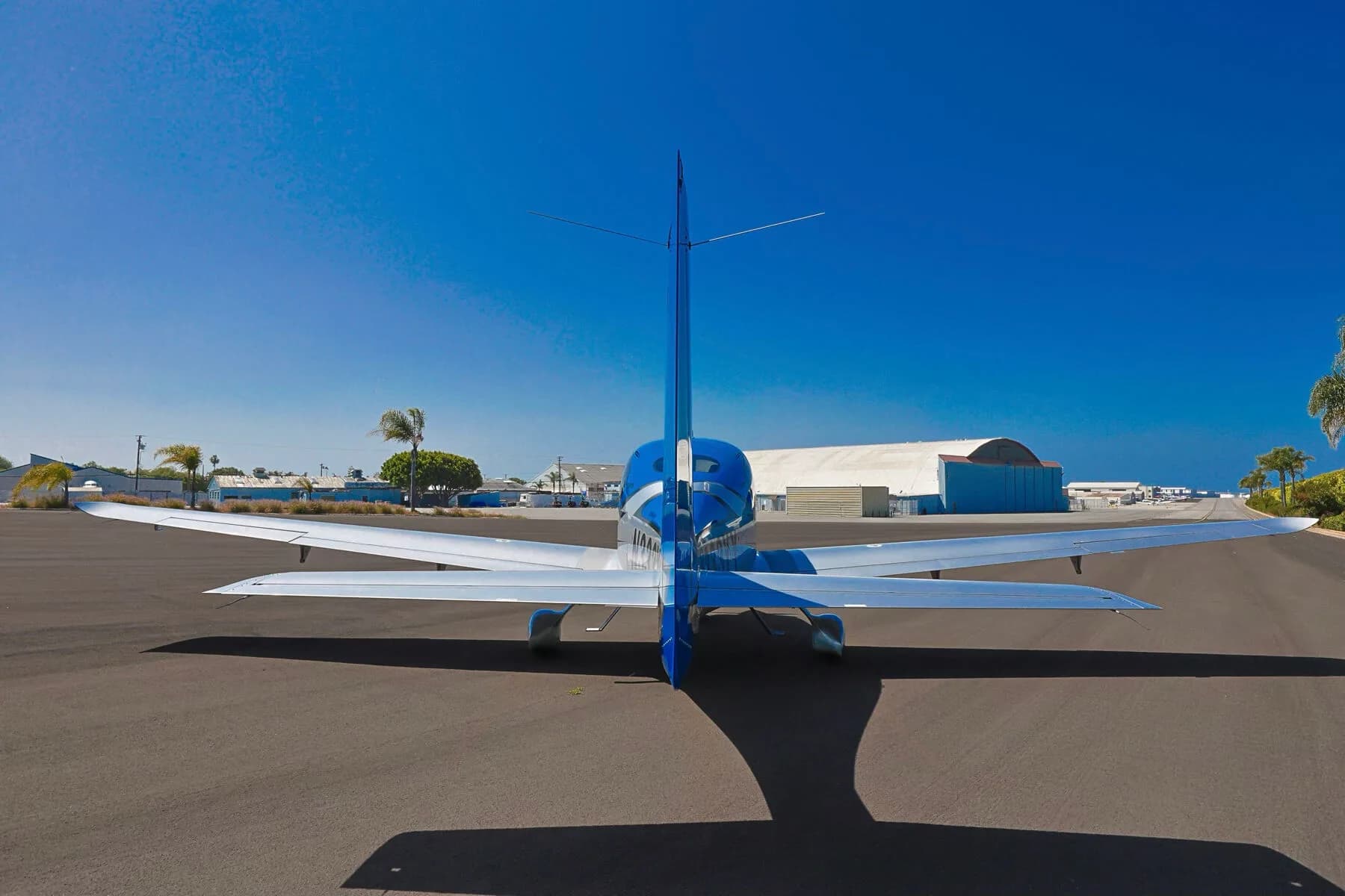 A rear view of the blue and silver Cirrus SR20 aircraft N333YY parked on an asphalt ramp with a hangar in the distance.