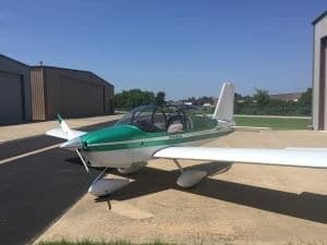 A white and green aircraft is parked outside a hangar on a sunny day.