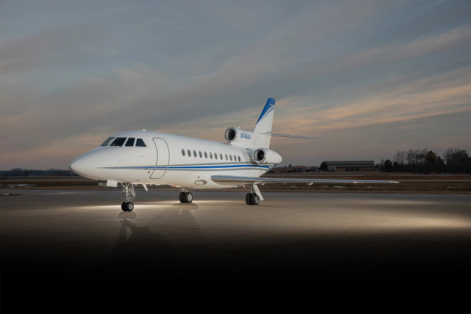 Front side view of a white and blue jet with registration N746AR on the tarmac at sunset.