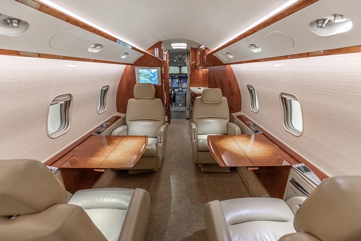 A view of the Challenger 350 cabin with beige leather seats and wood tables from the front.