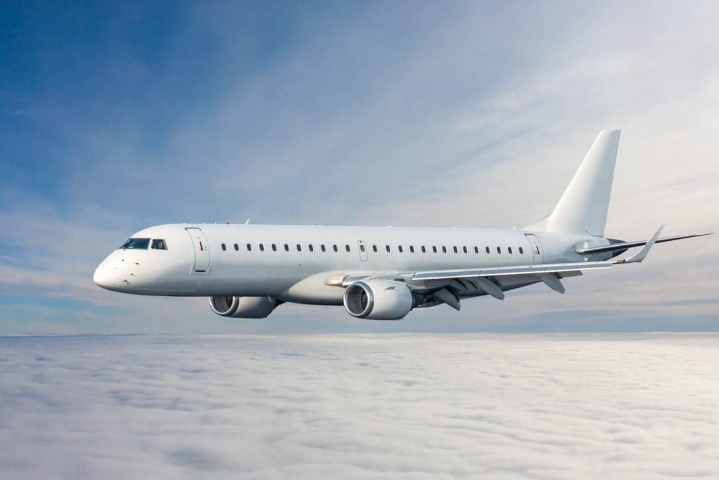 A white passenger jet flying above a layer of white clouds against a blue sky.