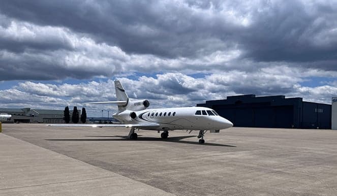 A white jet aircraft is parked on the tarmac under a cloudy sky.