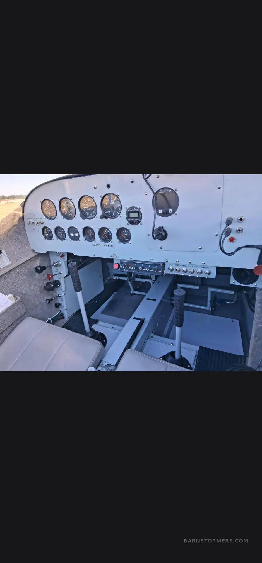 The cockpit of a small aircraft, showing the instrument panel with gauges and switches, and two control sticks.