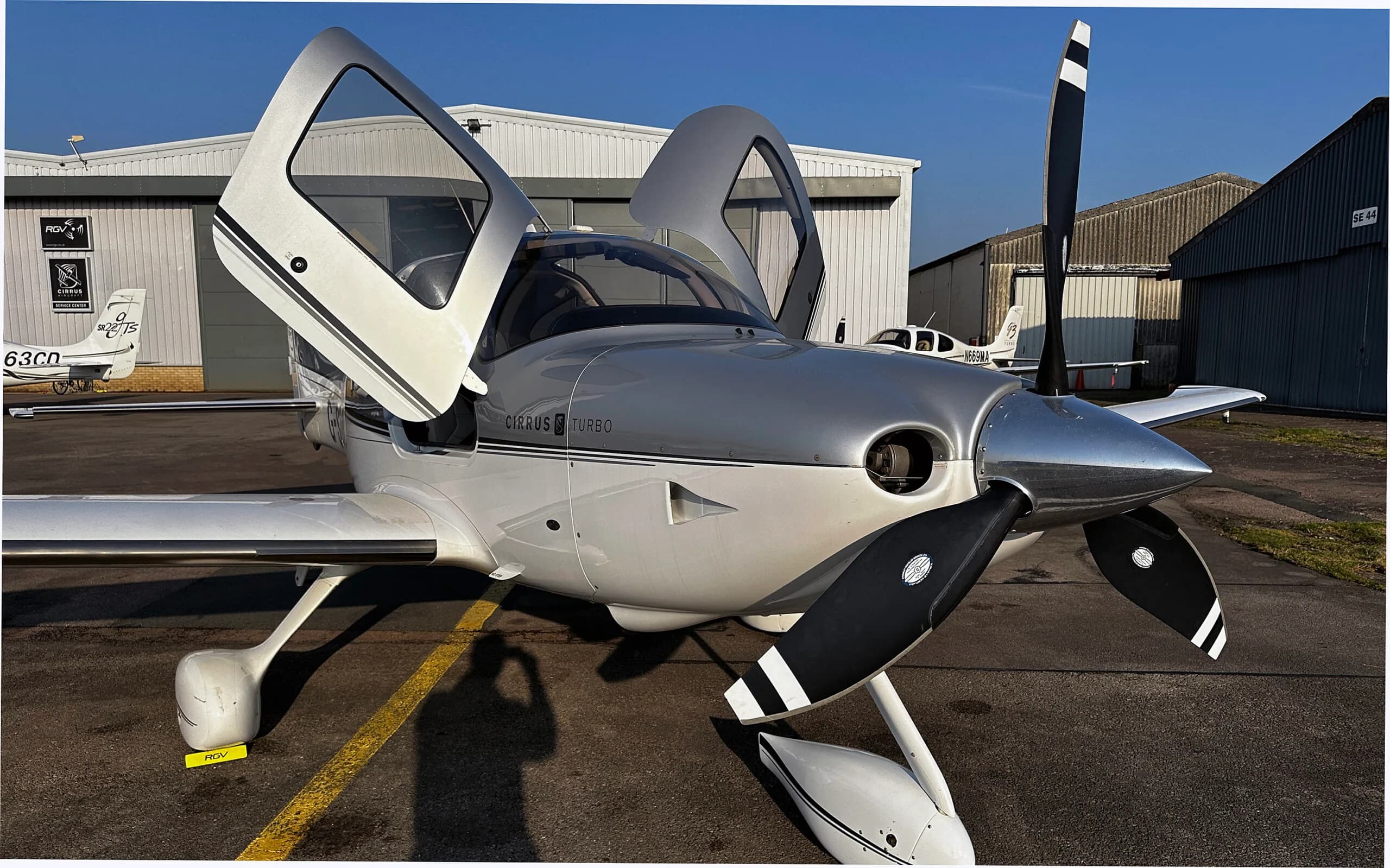 A silver and white Cirrus SR22 Turbo aircraft with its doors open, parked on an airfield.