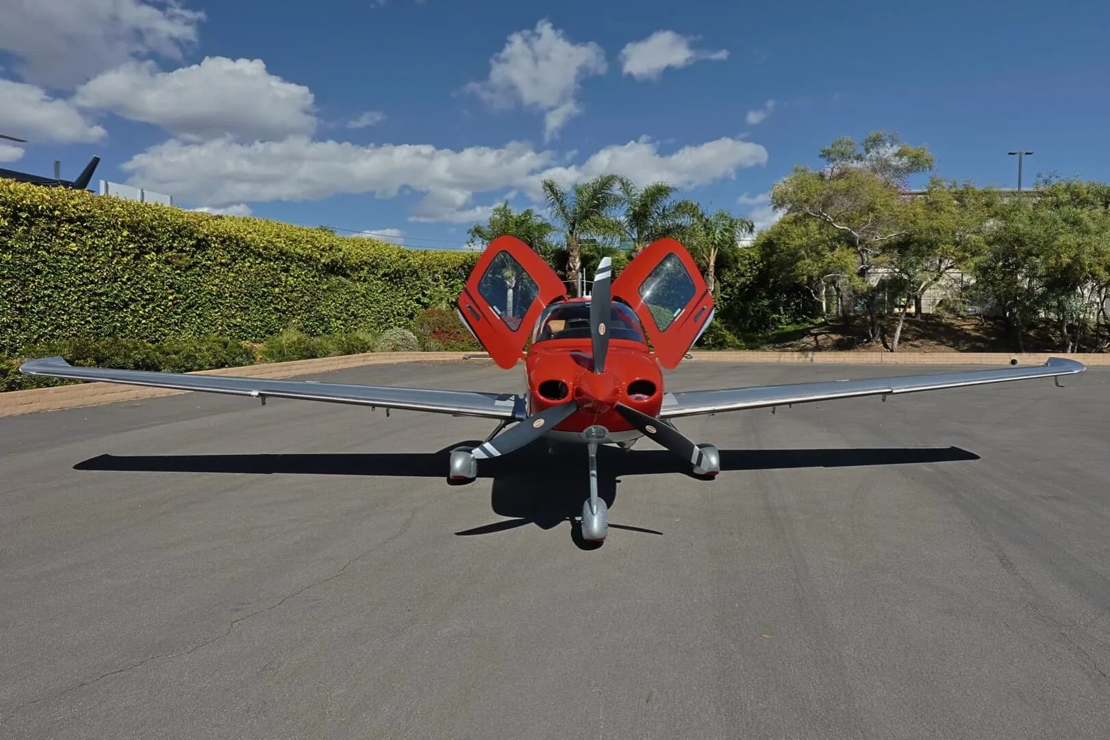 A front view of the red and silver Cirrus SR22 GTS aircraft, N245WP, with its gull-wing doors open.