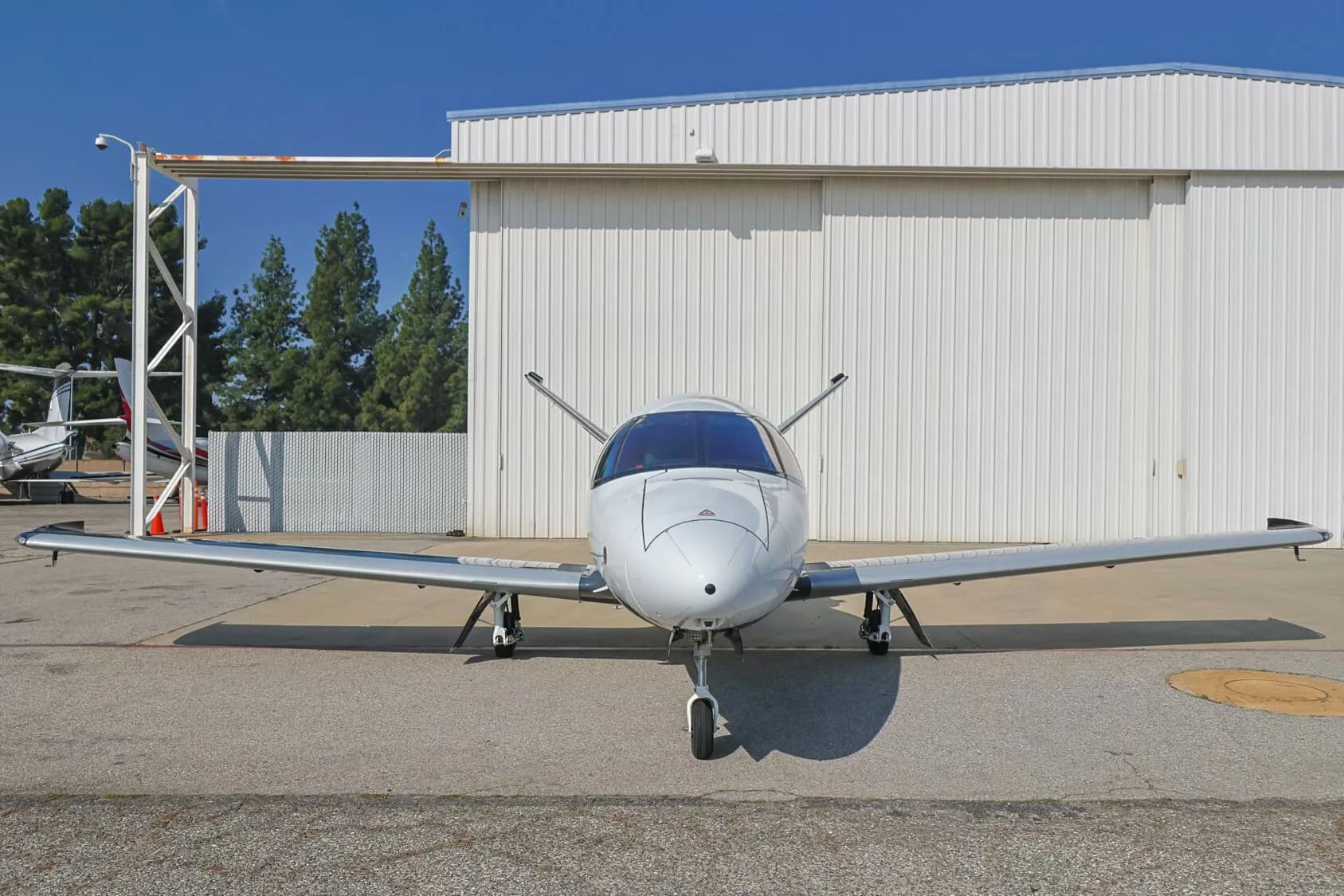 Front view of a white Cirrus Vision Jet parked on an tarmac in front of a hangar.