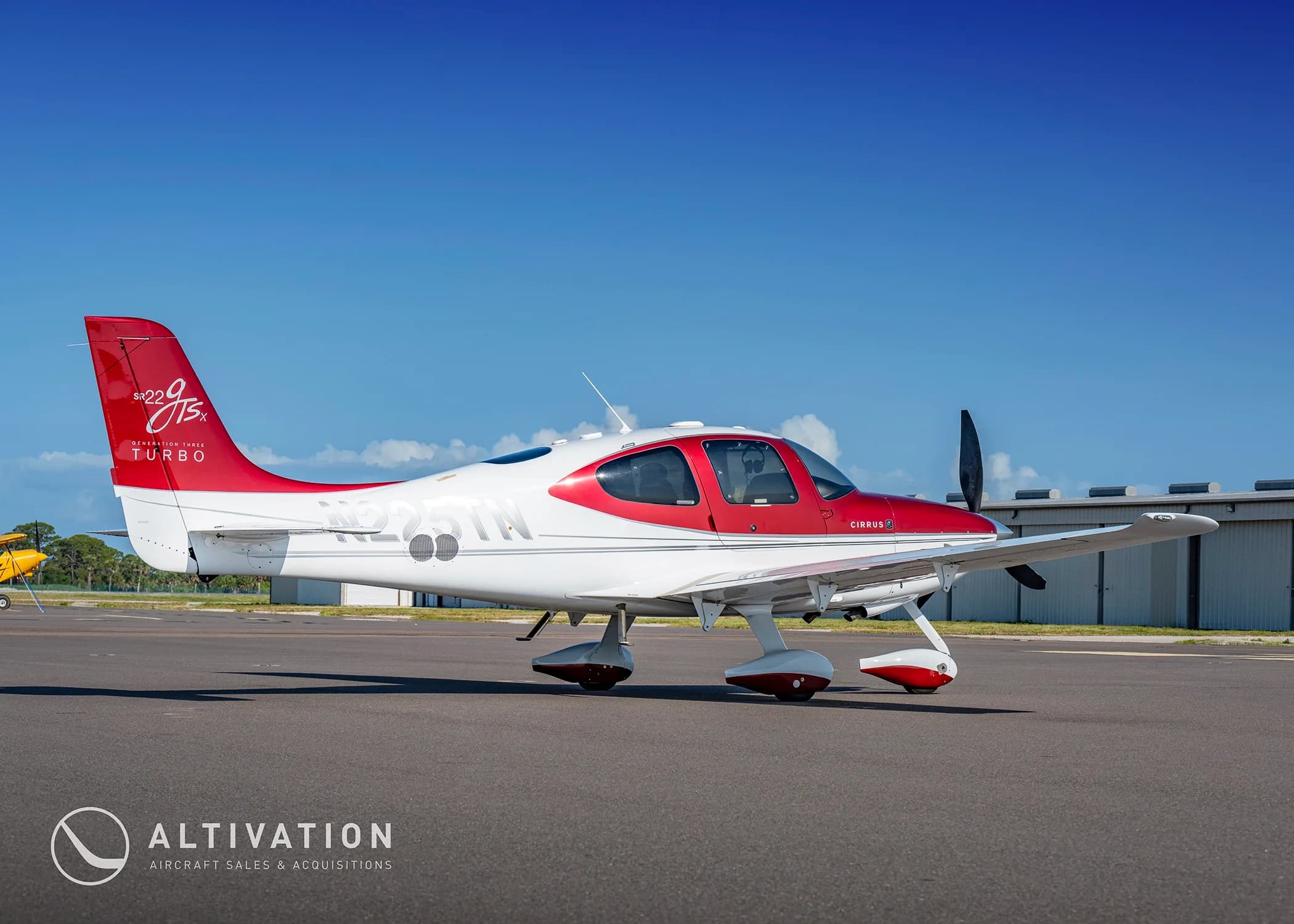 A side view of a red and white Cirrus SR22T aircraft (N225TN) parked on an airfield next to a hangar.