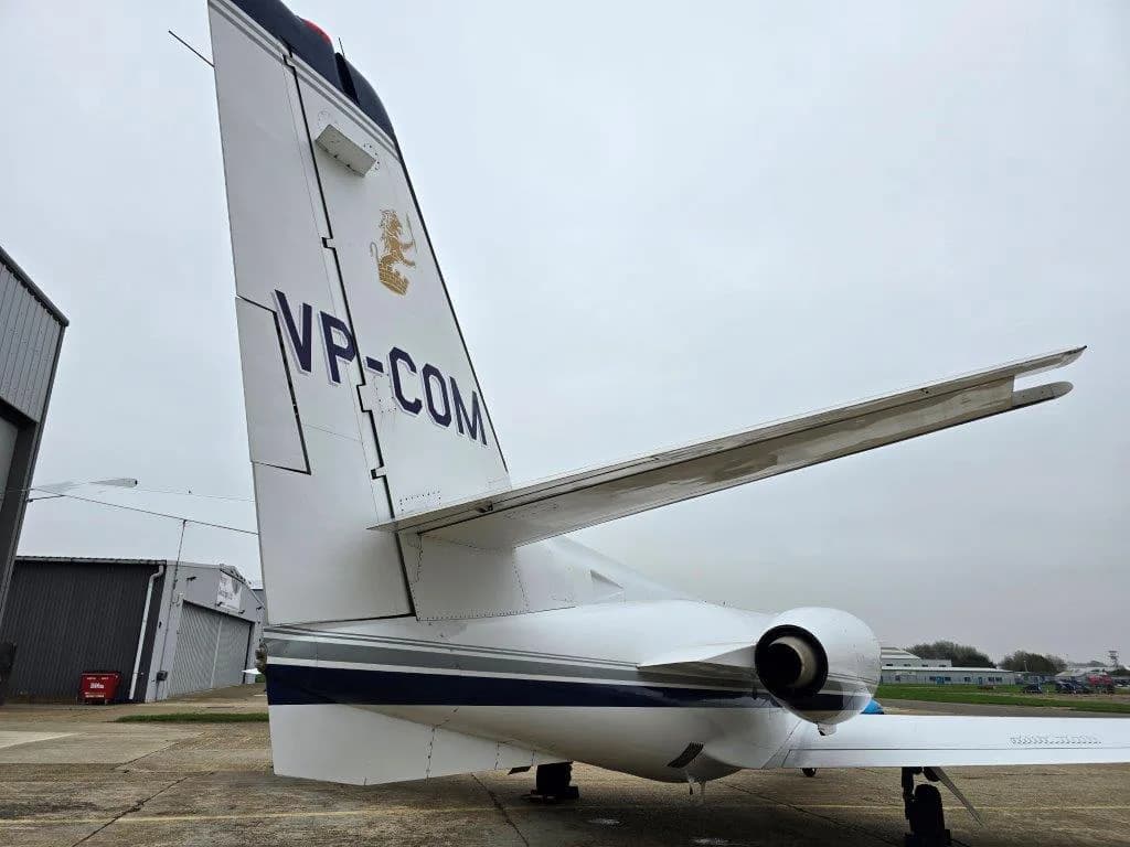 A close-up view of the tail section of a white Cessna Citation jet, showing the registration VP-COM and an engine exhaust.