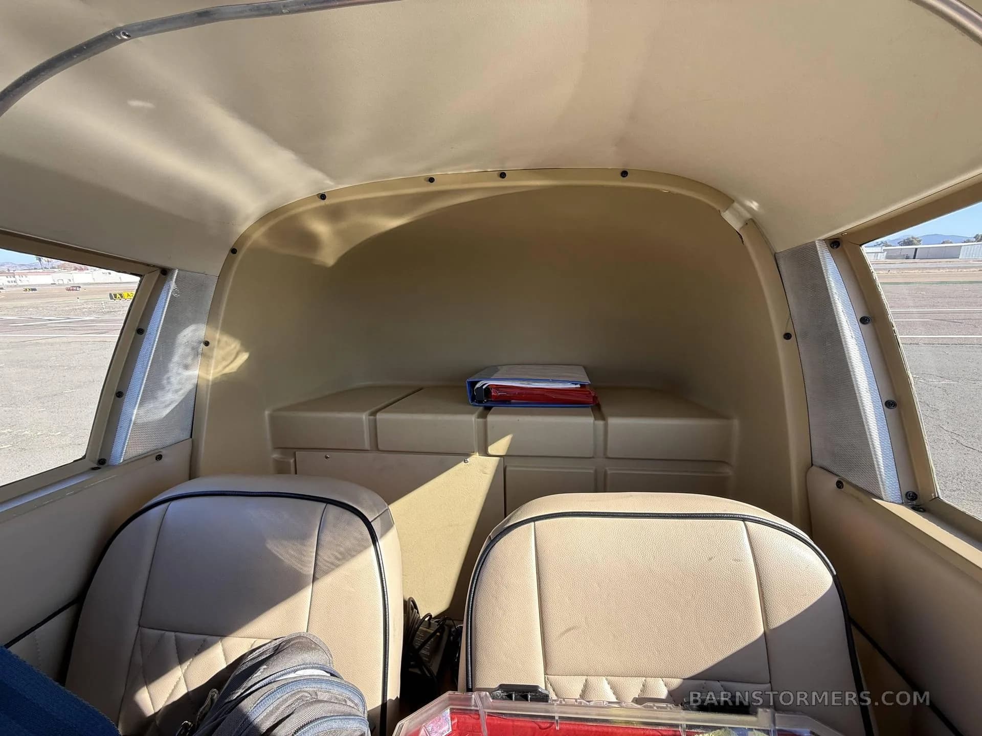 The tan interior cabin of a light aircraft, showing the two rear seats and baggage area.