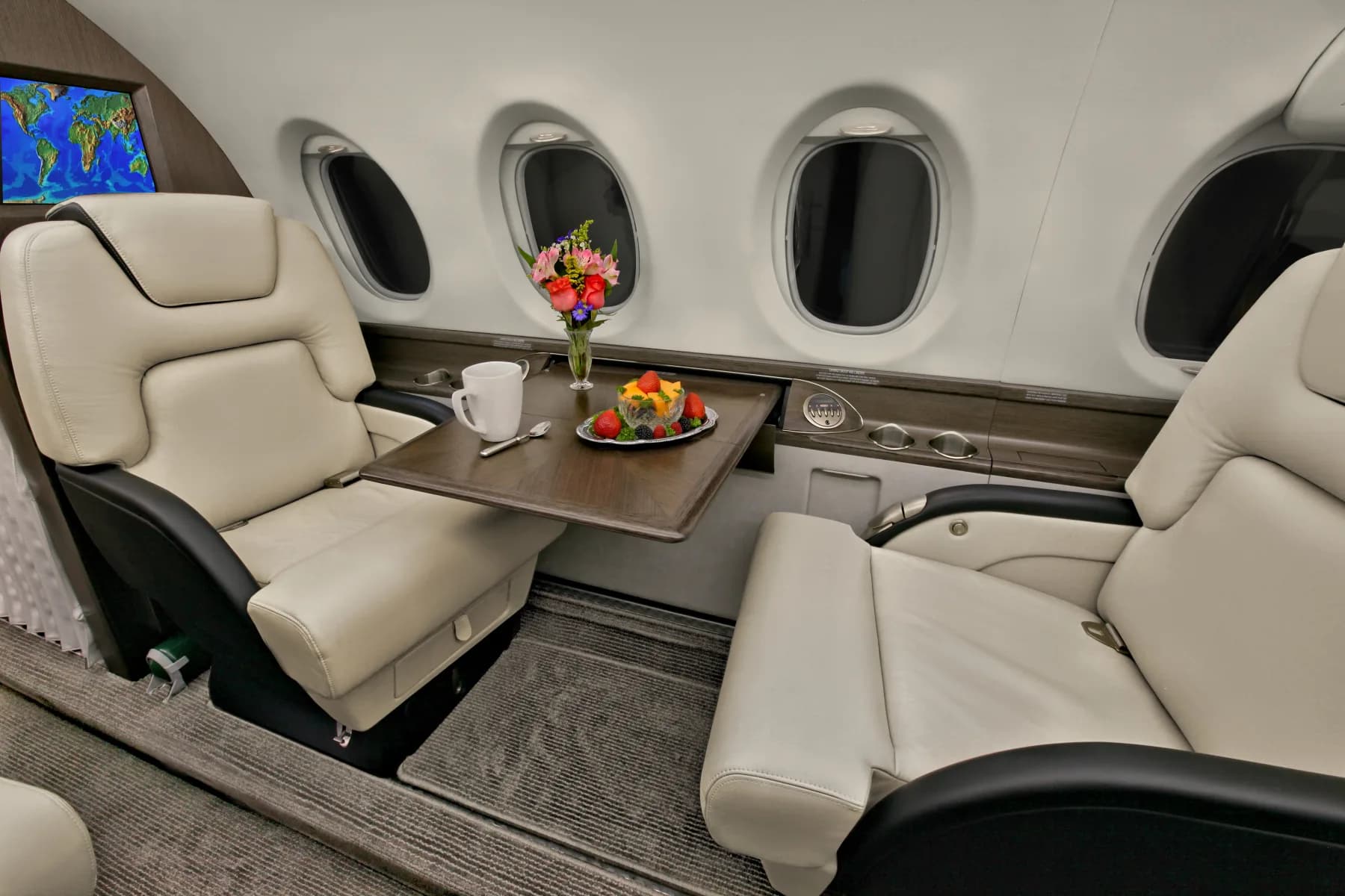 View of the aircraft's interior cabin with cream and black leather seats and a table with flowers and fruit.