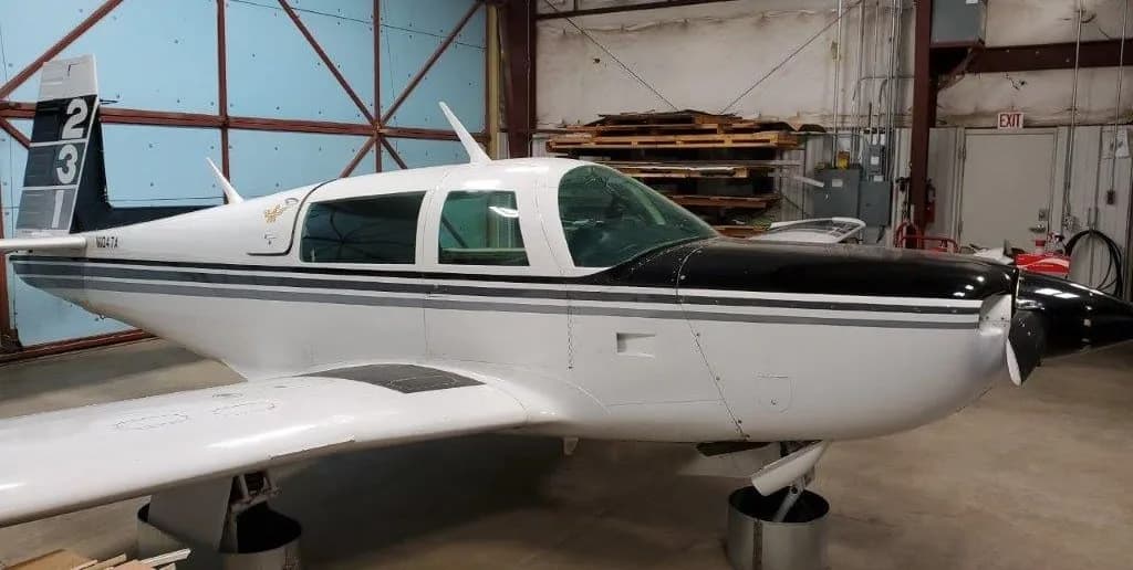 Front-side view of a white and black Grumman American AA-5 Traveler aircraft, N1047A, inside a hangar.