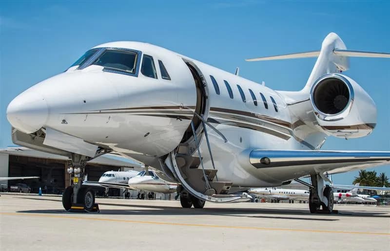 A white jet with brown stripes is parked on the tarmac with its door open.