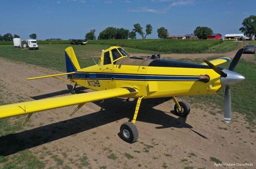 A yellow and blue Air Tractor AT-400 agricultural aircraft is parked in a field.