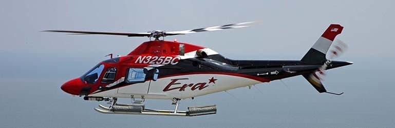 A red, white, and black Bell 407 helicopter with tail number N325BC in flight.