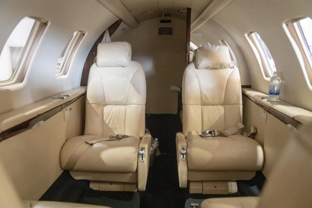 The interior cabin of a business jet with two rows of beige leather seats facing each other.