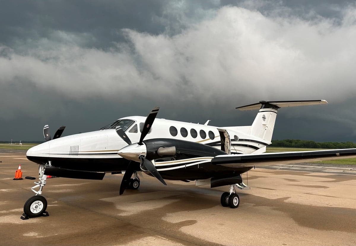 A King Air turboprop aircraft is parked on the tarmac with a stormy sky in the background.