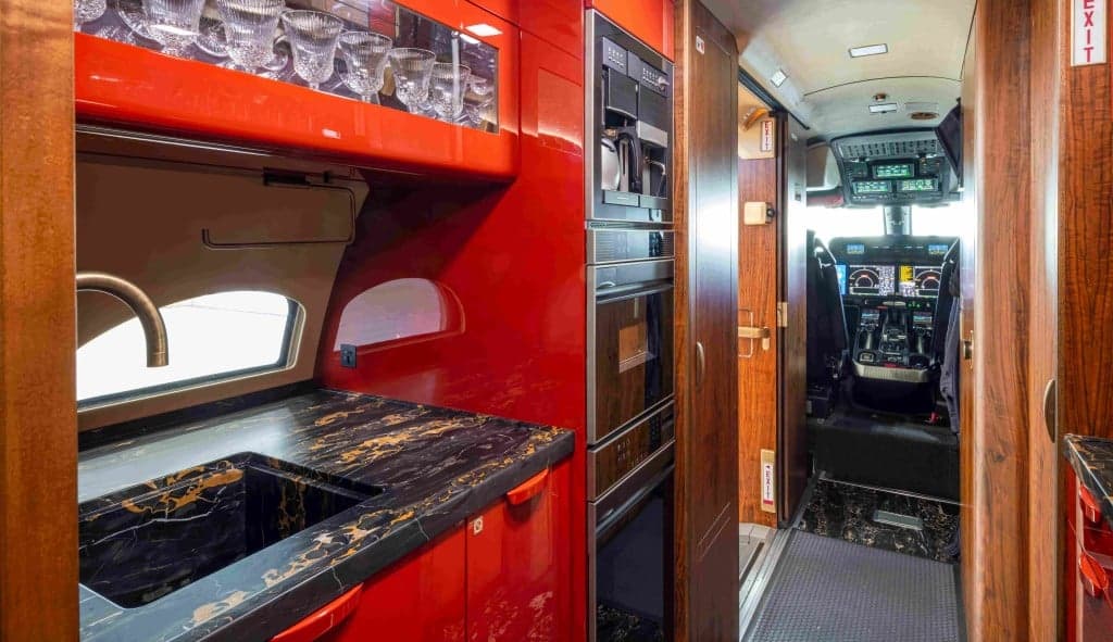 A view of the aircraft's cabin with tan leather seats and blue walls, looking towards the cockpit.