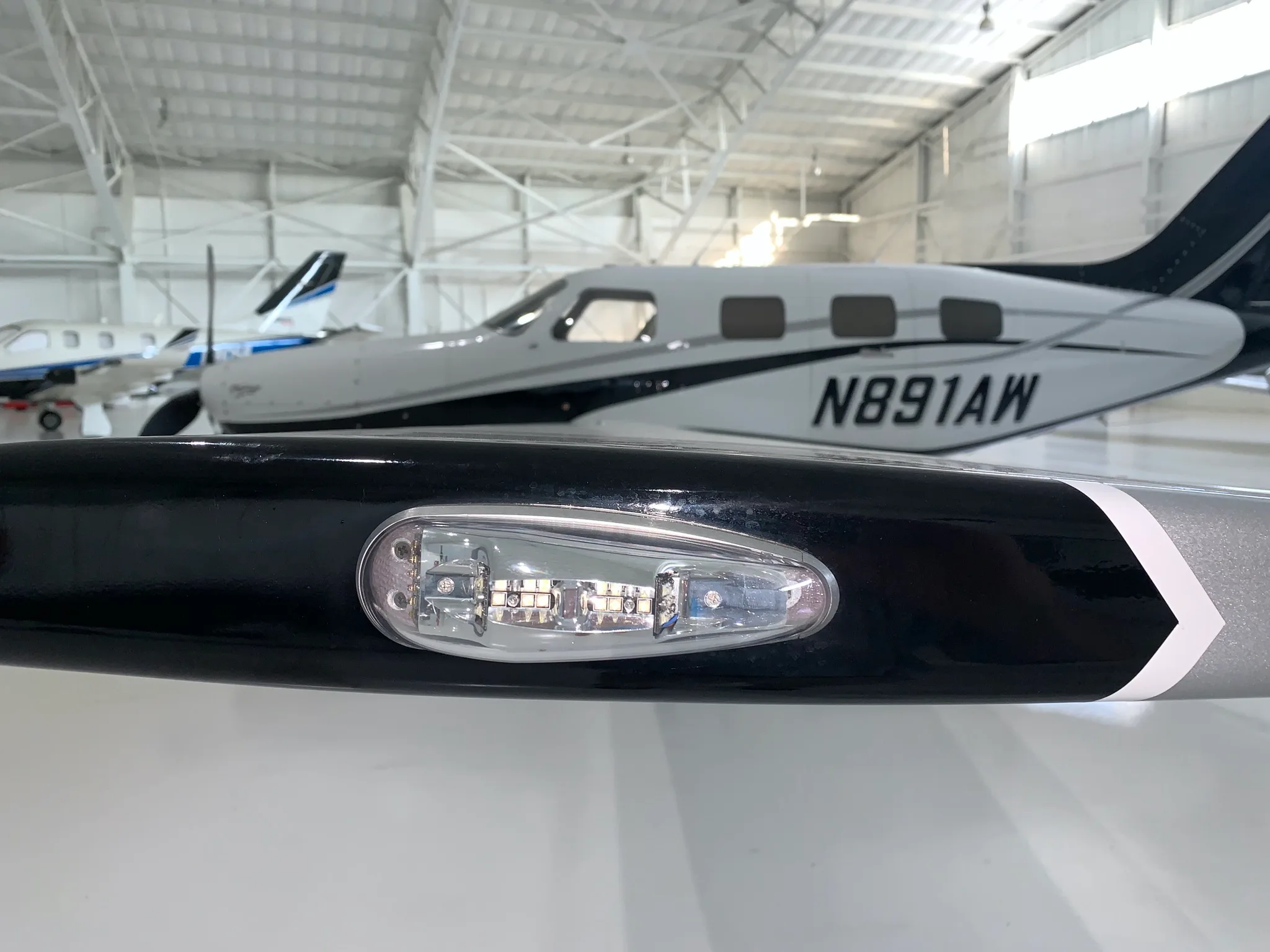 A close-up view of the wingtip light on a white and black Piper Mirage aircraft, with the fuselage visible in the background.