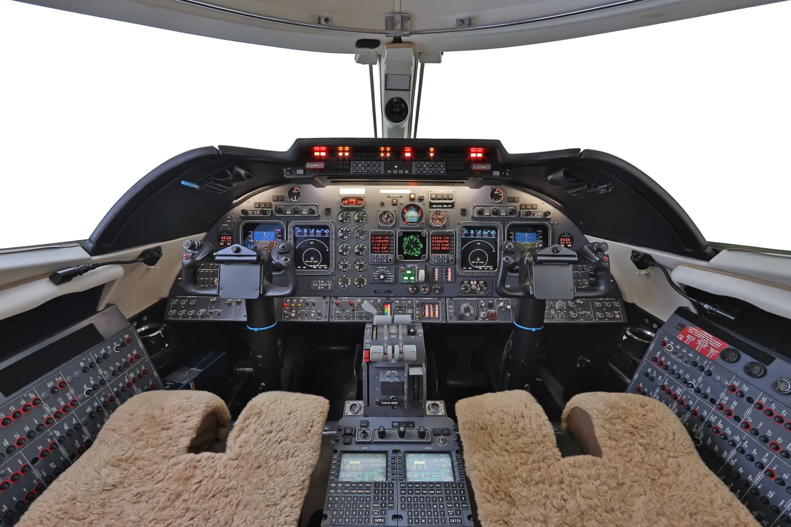 The cockpit of a business jet, featuring a complex instrument panel, control yokes, and sheepskin seat covers.
