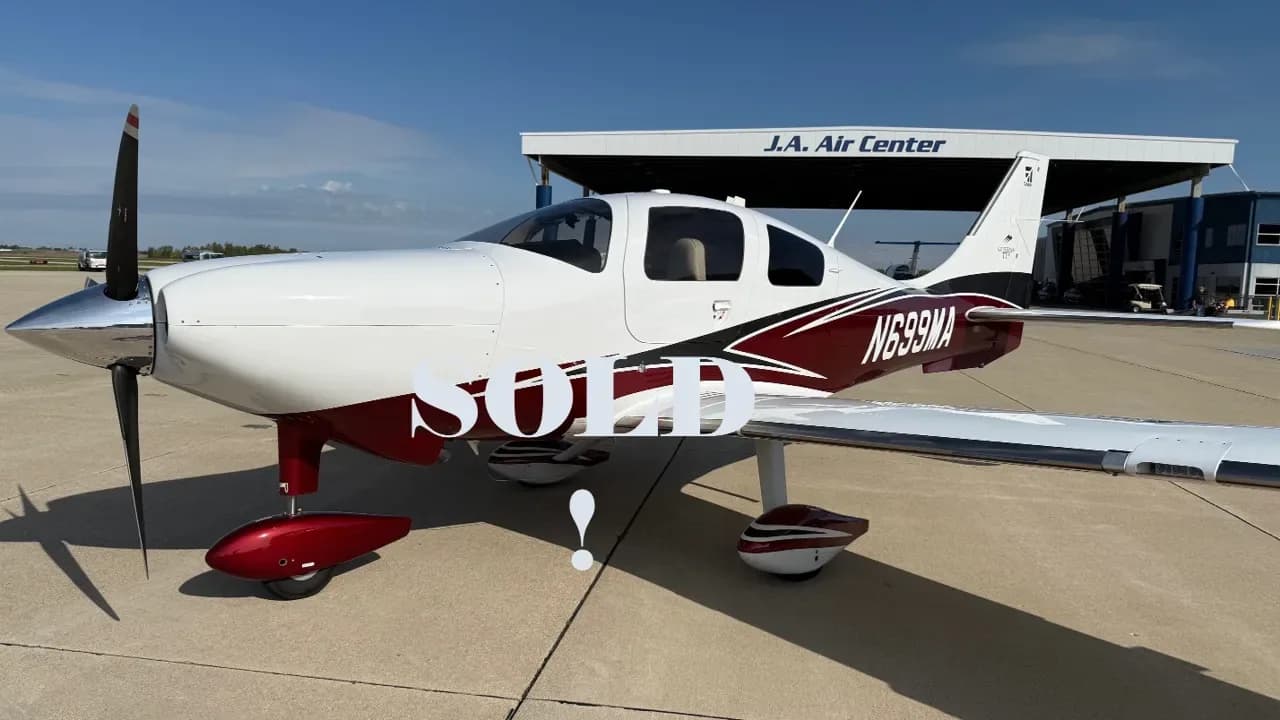 A white and maroon single-engine propeller aircraft with registration N699MA parked on a tarmac in front of a hangar.