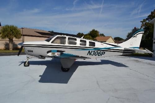 A Beechcraft Bonanza aircraft with a white and blue paint scheme parked on a concrete surface.