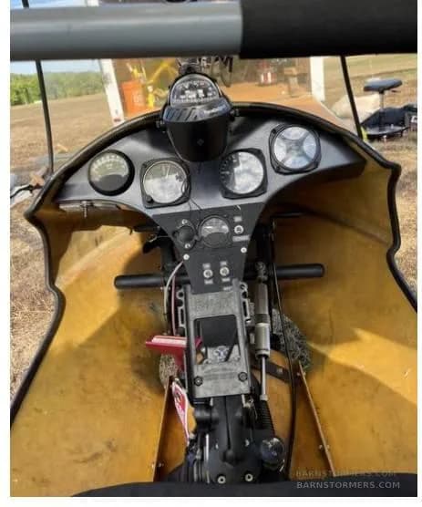 The cockpit of a yellow ultralight aircraft, showing the instrument panel with gauges and a compass.