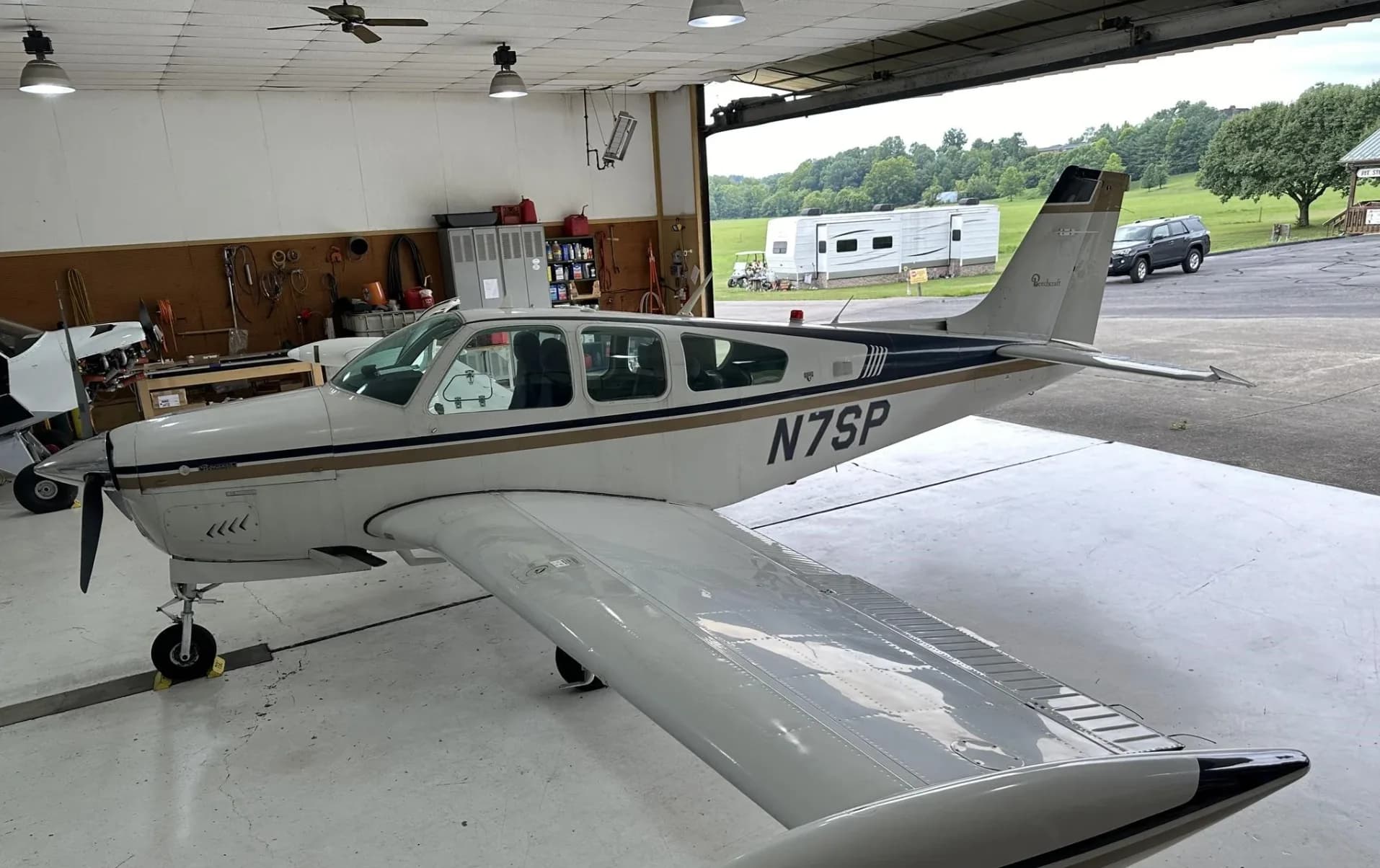 A white and gold Beechcraft Bonanza N7SP parked in a hangar, viewed from the rear right.