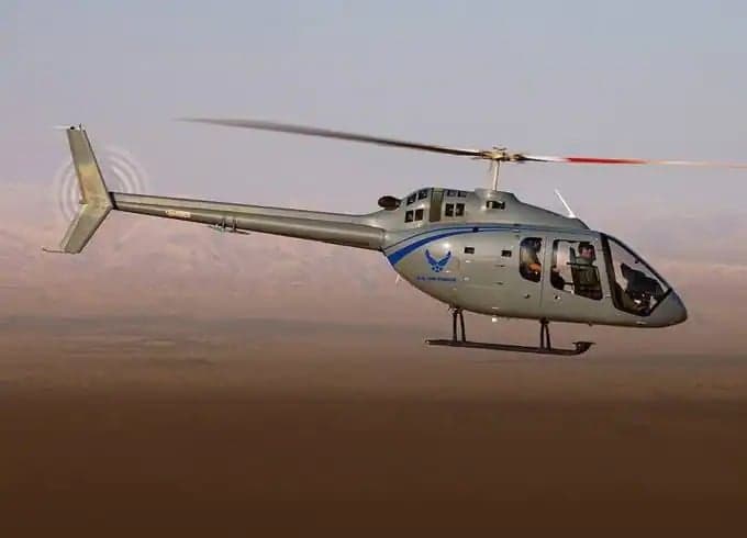 A gray helicopter with blue accents flies over a desert landscape.