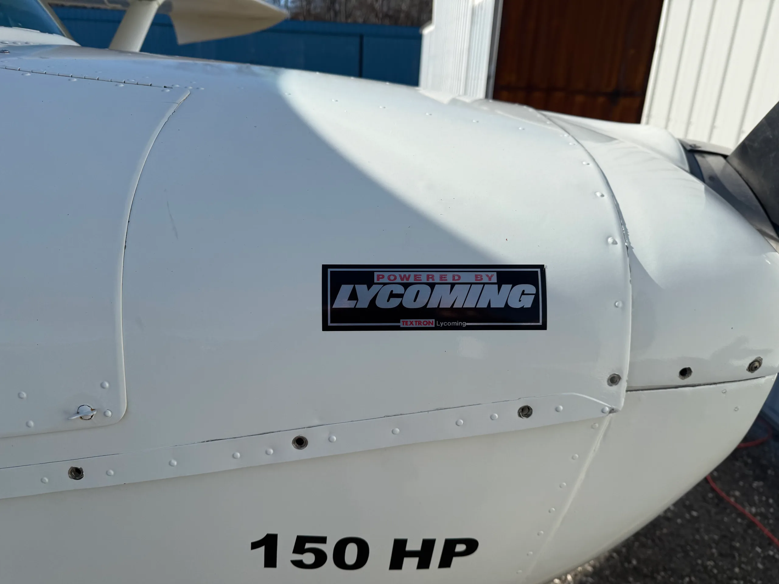 A close-up of the white engine cowling of a Cessna 150, showing "POWERED BY LYCOMING" and "150 HP" text.