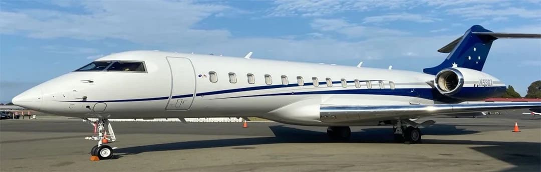 A white and blue Bombardier Challenger 605, N59GX, is parked on an airport tarmac under a blue sky.