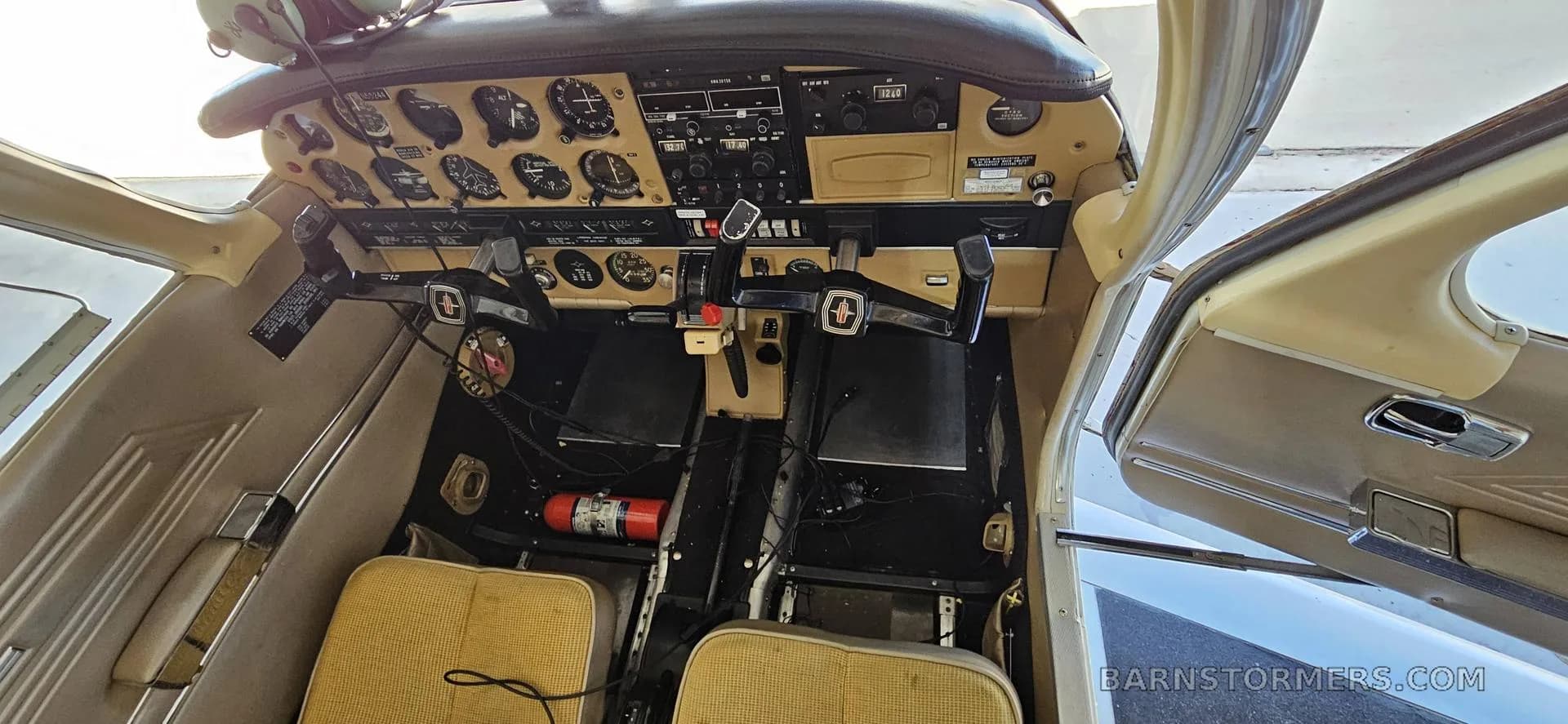 The cockpit of a light aircraft with a tan instrument panel, dual yokes, and various gauges.