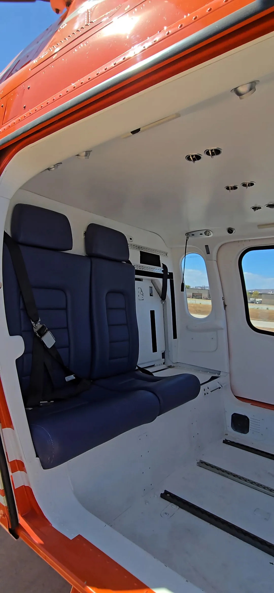The helicopter's interior cabin with two blue passenger seats and white walls.
