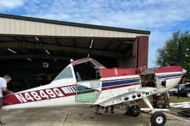 Red, white, and blue Air Tractor crop duster parked in front of a hangar with the door open.