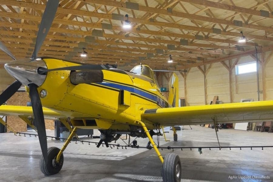 Close-up of the front of a yellow and blue agricultural aircraft in a hangar.
