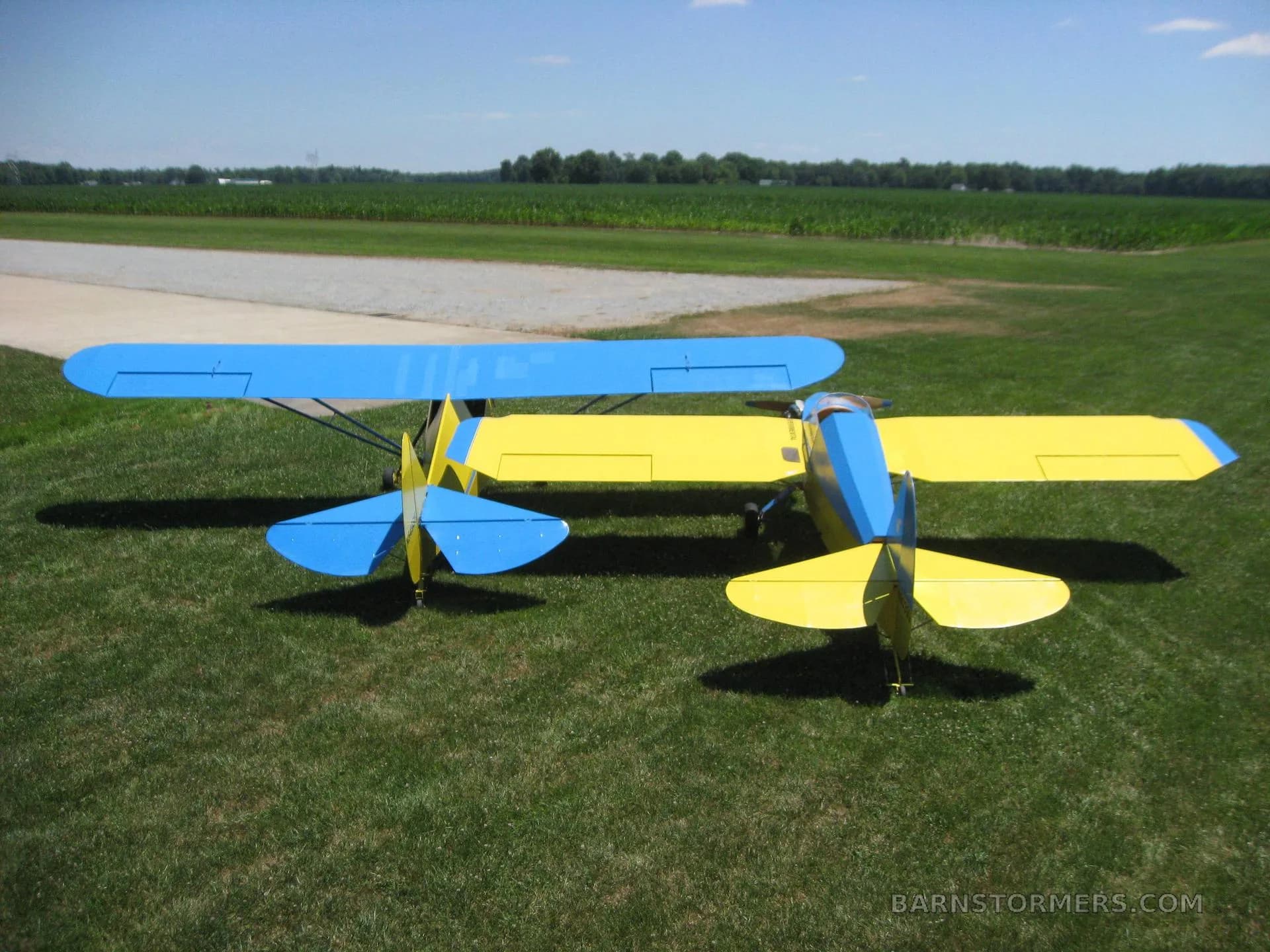 Overhead view of two yellow and blue single-engine aircraft parked on a grassy field.