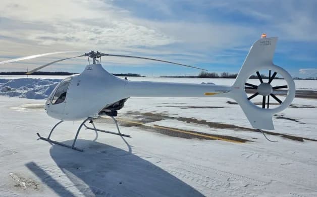 A white Guimbal Cabri G2 helicopter is parked on a snowy tarmac under a partly cloudy sky.