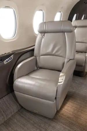 Aircraft cabin interior with leather seats and dark wood trim.