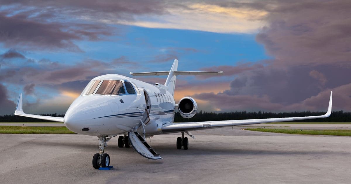 A white jet with an open door is parked on the tarmac at sunset.
